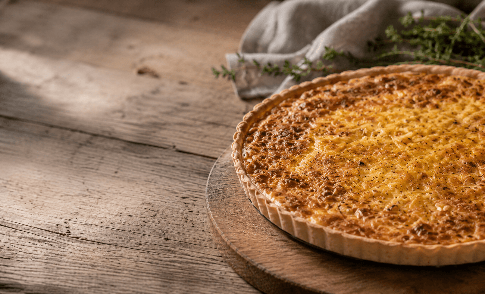 Freshly baked quiche on a wooden board with herbs and linen